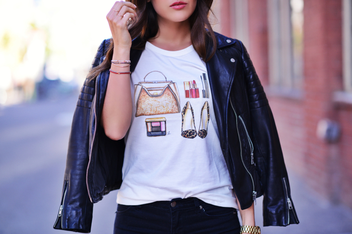 Close up of a graphic tee, colorful bracelets and black leather jacket. 