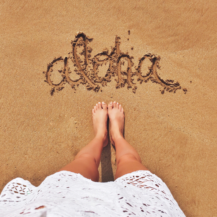 blank itinerary feet in the sand with aloha written in the sand.