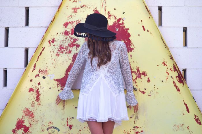 Blank Itinerary leaning on the wall wearing a black hat and white lace dress
