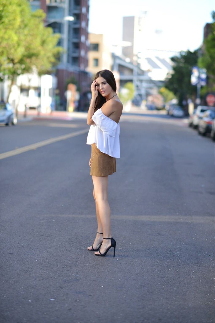 Standing in the middle of the streets of San Diego wearing white top, suede skirt and black heels