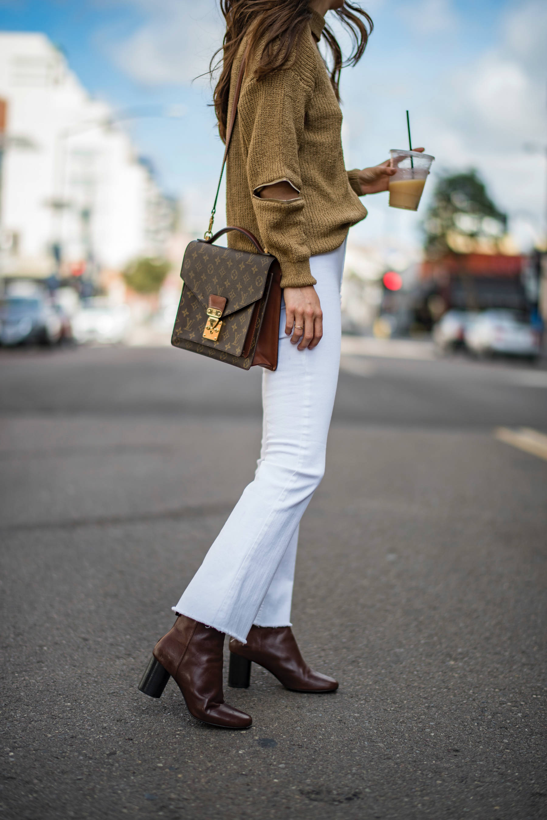 Close-up of the details of the blogger's outfit, showing a brown Louis Vuitton purse, white flare jeans and brown boots.