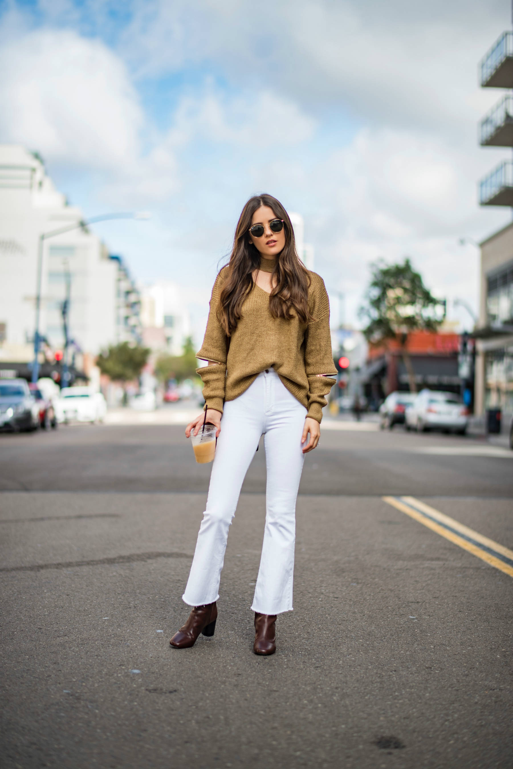 Blogger, Blank Itinerary posing for a photo in the middle of the street wearing white flare jeans and brown fall sweater.