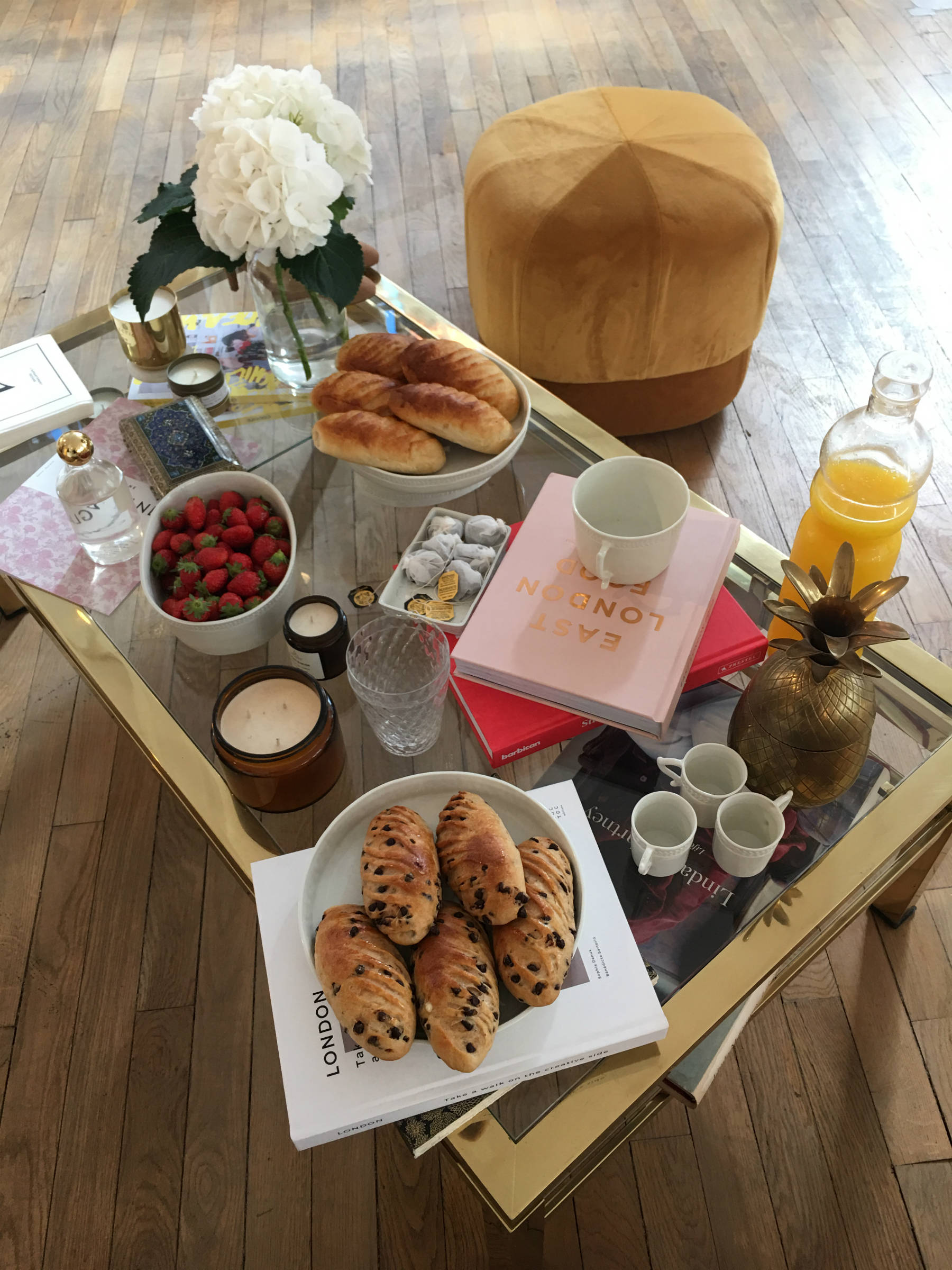 Coffee table with croissants, strawberries, orange juice, white peonies and books.