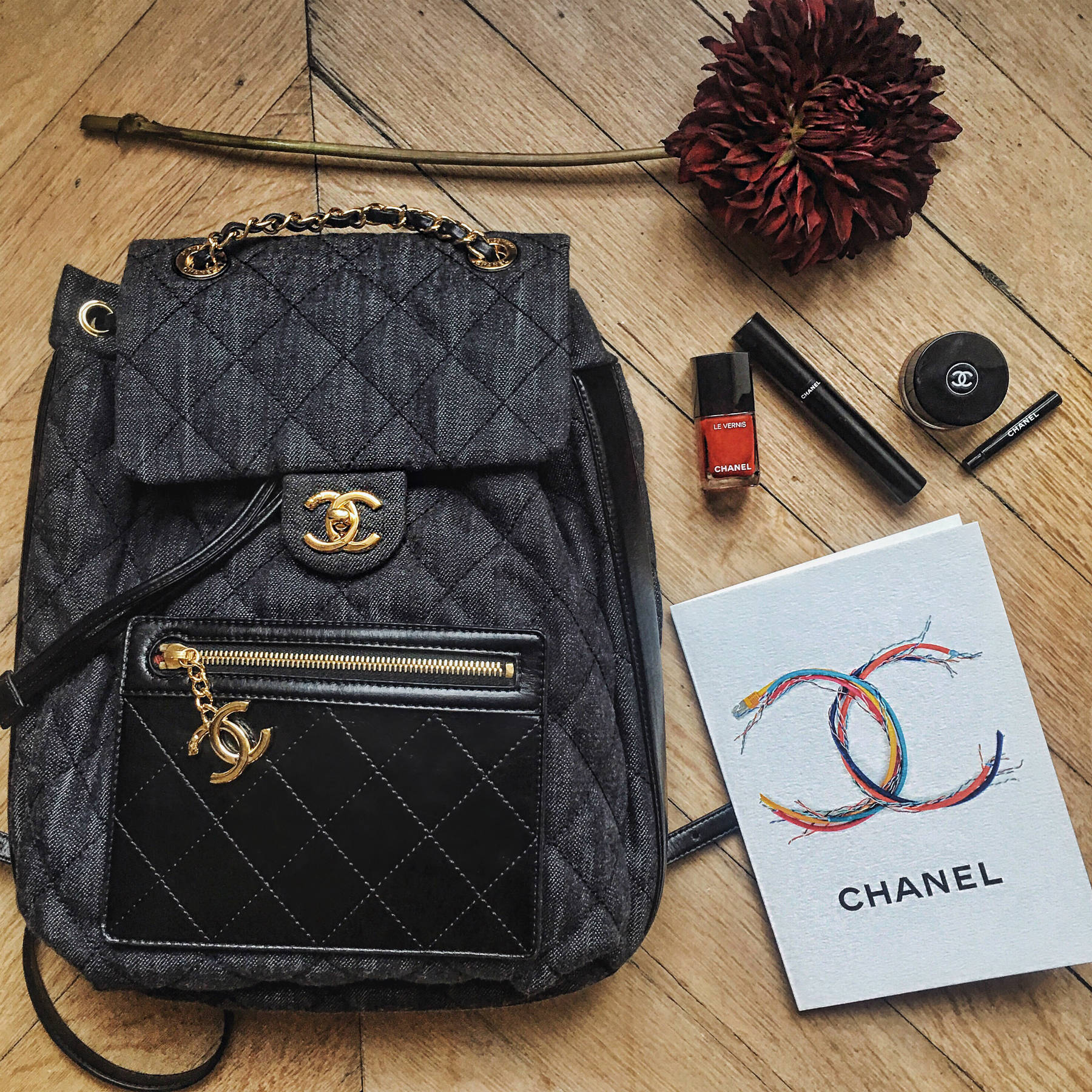 Layout of a Chanel backpack and lipstick and makeup on a table.
