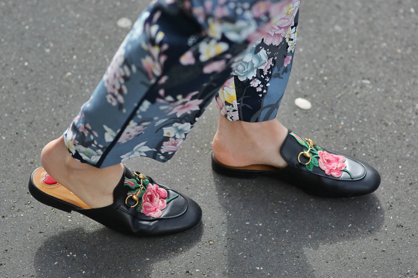 Close-up shot of black Gucci loafer mules with pink embroidered flower.